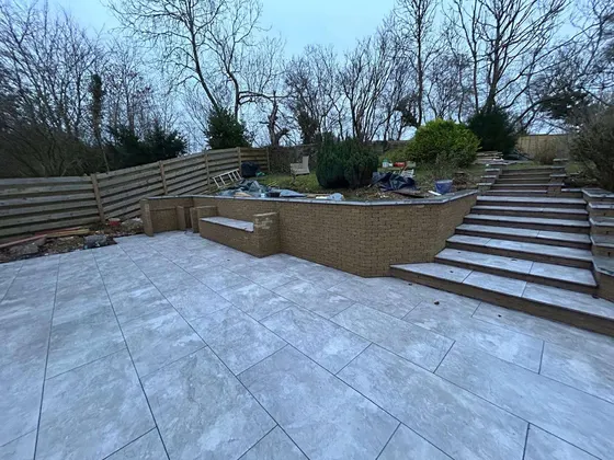 Large grey porcelain terrace with wide steps up to a raised garden