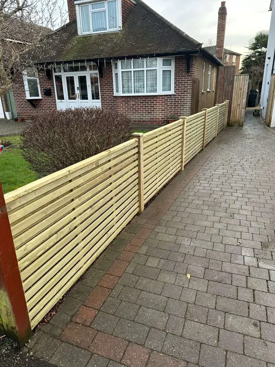 New horizontal slatted fence running alongside a block-paved front path
